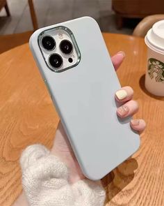 a woman holding up her phone case on top of a wooden table next to a cup