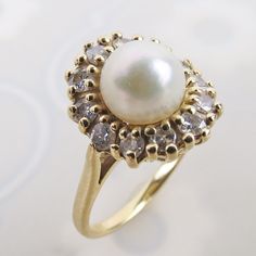 "A lovely natural white pearl tops this elegant 14k yellow gold diamond halo ring. The white lustrous pearl sits 7/16 inch tall above the finger. A row of twelve tiered 2mm .03 carat diamonds flow around the pearl. The dazzling gemstones top a linear wire gallery and smooth sturdy band.  The inside is stamped \"14k\" (gold purity) with no other identifying hallmarks. The ring has an estimated total weight of .36 carat diamonds.  The ring measures an approx. petite size 4.75 and could be re-sized Luxury Formal Pearl Ring With Halo Design, Timeless Pearl Ring With Diamond Accents For Anniversary, Timeless Anniversary Pearl Ring With Diamond Accents, Elegant Pearl Ring With Diamond Center Stone, Timeless Diamond-white Pearl Ring With Diamond Accents, Classic Oval Pearl Ring With Diamond Accents, Timeless Diamond White Pearl Ring With Diamond Accents, Timeless Diamond Pearl Ring With Center Stone, Classic Pearl Ring With Diamond