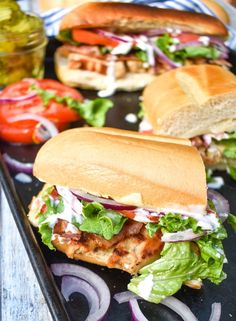 two sandwiches with lettuce, tomatoes and onions on a tray next to pickles