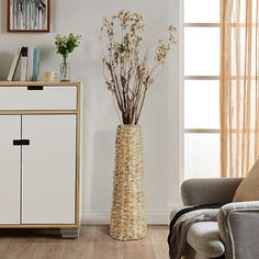 a tall vase with flowers in it sitting on a table next to a gray chair