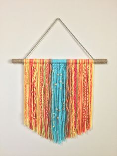 a multicolored wall hanging on a white wall with string and wooden pegs