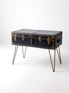 an old trunk sitting on top of a metal stand with four drawers and two legs