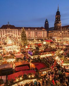 an outdoor christmas market with lots of lights and trees in front of large buildings at night