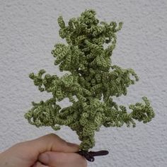 a hand holding a small crocheted plant in front of a white wall