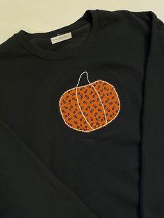 This charcoal sweatshirt is a unisex with a hand embroidered pumpkin in fabric applique on the front chest area. Orange with black floral pumpkin. Black Tops With Embroidered Graphics For Fall, Black Embroidered Tops For Fall, Black Embroidered Cotton Sweater, Black Embroidered Tops For Halloween, Black Cotton Embroidered Sweater, Black Cotton Sweatshirt For Fall, Black Embroidered Sweater For Fall, Long Sleeve Tops With Embroidered Patch For Fall, Black Cotton Sweater With Embroidered Graphics