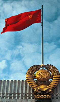 two flags flying in front of a building with a red and gold flag on top