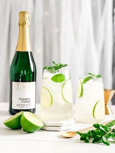 two glasses filled with ice and limes next to a bottle of wine