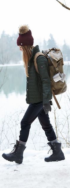 a woman walking in the snow with a backpack on her back and boots off to the side