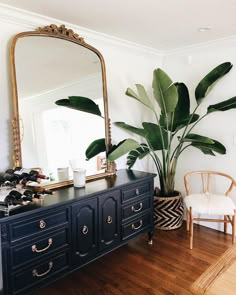 a large mirror sitting above a dresser in a living room next to a chair and potted plant