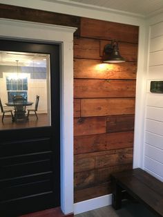 a wooden wall with a black door and bench in front of it on the side of a house