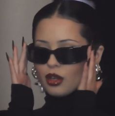 a woman wearing sunglasses and holding her hands up to her face