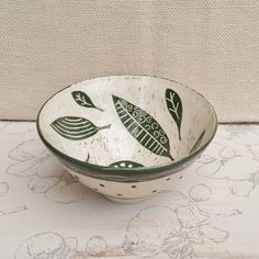 a white bowl with green designs on it sitting on a table next to a wall