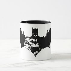 a batman silhouette on a white and black coffee mug with cityscape in the background