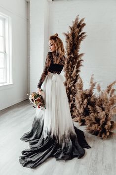 a woman is standing in front of some plants wearing a black and white wedding dress