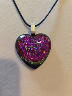 Pretty black resin heart pendant with crushed glass in purple and green tones with hints a teal. Silver toned alloy bail with an 18" black, waxed cotton necklace that has a 2" extender attached. Comes to you sealed in protective wrap in a cute gift box. Handmade Iridescent Jewelry For Valentine's Day, Heart Beads Resin Jewelry Gift, Black Heart-shaped Necklace For Keepsake, Black Heart Necklace For Keepsake, Black Heart Necklaces For Keepsake, Resin Jewelry With Glitter For Gift, Handmade Black Heart Necklace For Gift, Glitter Resin Jewelry For Gift, Glitter Resin Jewelry As A Gift