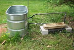 a metal barrel sitting in the grass next to a water pump and some other items