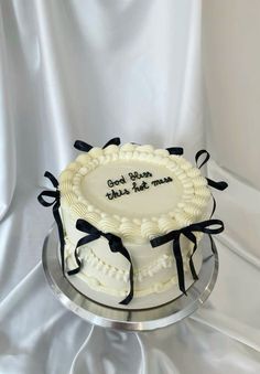 a white cake with black ribbon on top is sitting on a silver platter that says, we are the good times for this cake