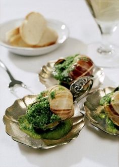 three silver dishes filled with food on top of a table next to wine glasses and utensils