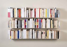 a bookshelf filled with lots of books on top of a wall next to a white wall