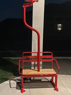 a red chair sitting on top of a cement block next to a white pillar and grass