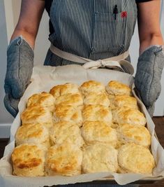 a person in an apron is holding a tray of biscuits