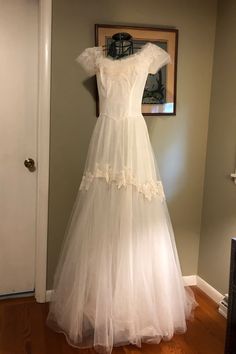 a white dress hanging on the wall in front of a door with a framed photo behind it