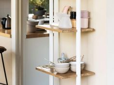 three wooden shelves with bowls, cups and utensils on them in a kitchen