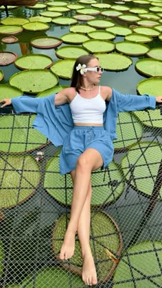 a woman sitting on top of a net over water lilies with her arms outstretched