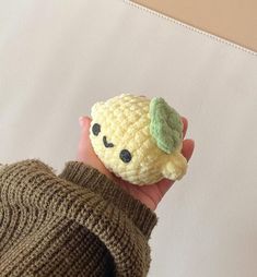 a hand holding a small crocheted toy with a green leaf on it's head