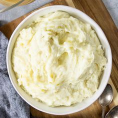 a white bowl filled with mashed potatoes on top of a wooden cutting board