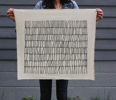 a woman holding up a piece of art with lines drawn on it in front of her