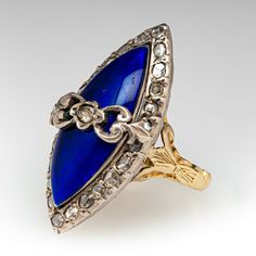 This beautiful mid-Victorian ring is centered with one (1) rose cut diamond bead set into a sterling silver setting set against navette shaped blue enamel dome and encircled with twenty-four (24) rose cut diamonds bead set into sterling silver settings. The under-gallery and the engraved shaped are constructed of 18K yellow gold. The ring measures 27.0mm at the top, rises 10.0mm above the finger, tapering to 2.6mm wide and 1.0mm thick at the base of the shank. This ring is currently a size 2.75. Elegant Wedding Enamel Ring With Rose Cut Diamonds, Formal Fine Jewelry Jeweled Rings, Elegant Jeweled Oval Rings, Elegant Oval Jeweled Rings, Elegant Enamel Ring With Rose Cut Diamonds For Wedding, Victorian Jewelry With 17 Jewels In Marquise Cut, Victorian Marquise Jewelry For Formal Occasions, Formal Victorian Jewelry With Marquise Shape, Antique Blue Diamond Ring For Formal Occasions