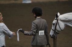 a woman standing next to a man holding a white horse's bridle