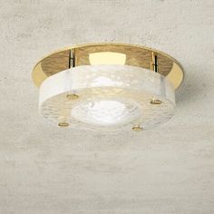 a white and gold ceiling light in a room with concrete wall behind the light fixture