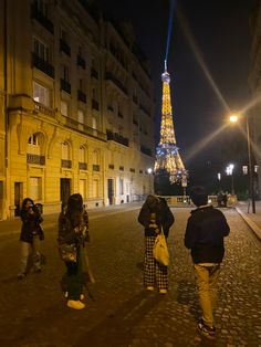 people are walking down the street in front of the eiffel tower at night