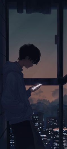 a man standing in front of a window looking at his cell phone while the sun is setting