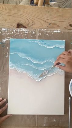 someone is painting waves on the beach with blue and white paint, while another person holds a brush in their left hand