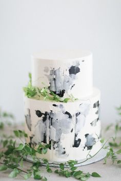 a three tiered cake with black and white paint splattered on it, surrounded by greenery