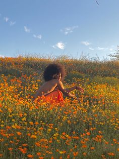 a woman in an orange dress sitting in a field of wildflowers with a kite flying above her