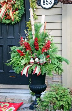 a black vase with red and white flowers in front of a door decorated for christmas