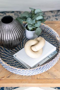 a coffee table with books and a vase on it, sitting next to a plant