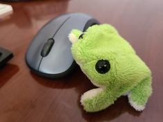 a green stuffed animal sitting next to a computer mouse