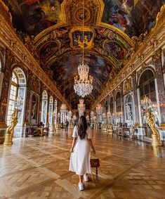 a woman in a white dress is walking through an ornate hall with paintings on the ceiling