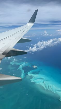 an airplane wing flying over the ocean and landforms in the distance with blue water below