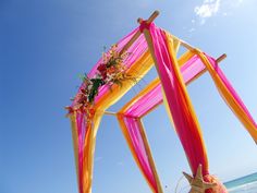 an outdoor wedding setup on the beach with pink and yellow draping, flowers and candles