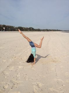 a woman doing a handstand on the beach