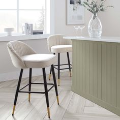 two white bar stools sitting in front of a counter with flowers on the table