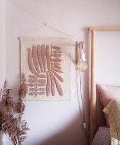 a wall hanging on the side of a bed next to a plant and a lamp