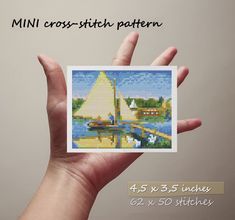 a hand holding a small cross - stitch pattern for a sailboat on the water