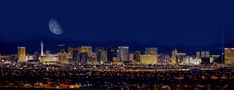 the city skyline is lit up at night, with mountains in the back ground and lights on